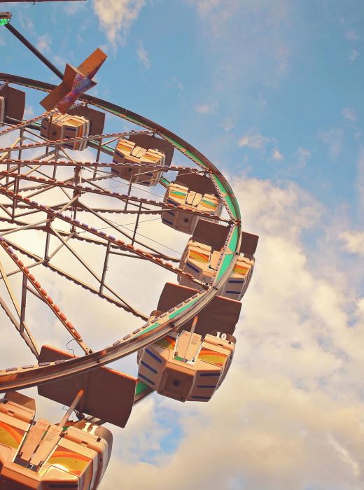 Ferris wheel against a blue sky with scattered clouds, viewed from below at an angle.