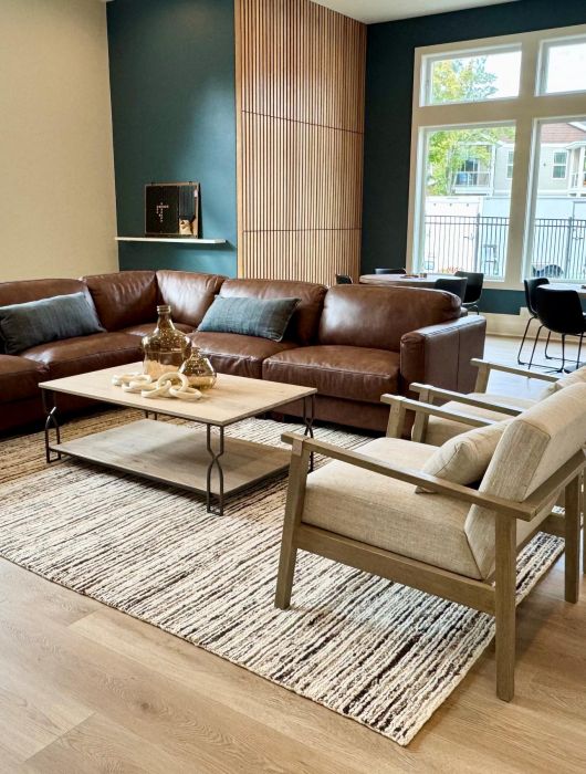 Modern living room with brown leather sofa, armchairs, coffee table, and large windows letting in natural light.