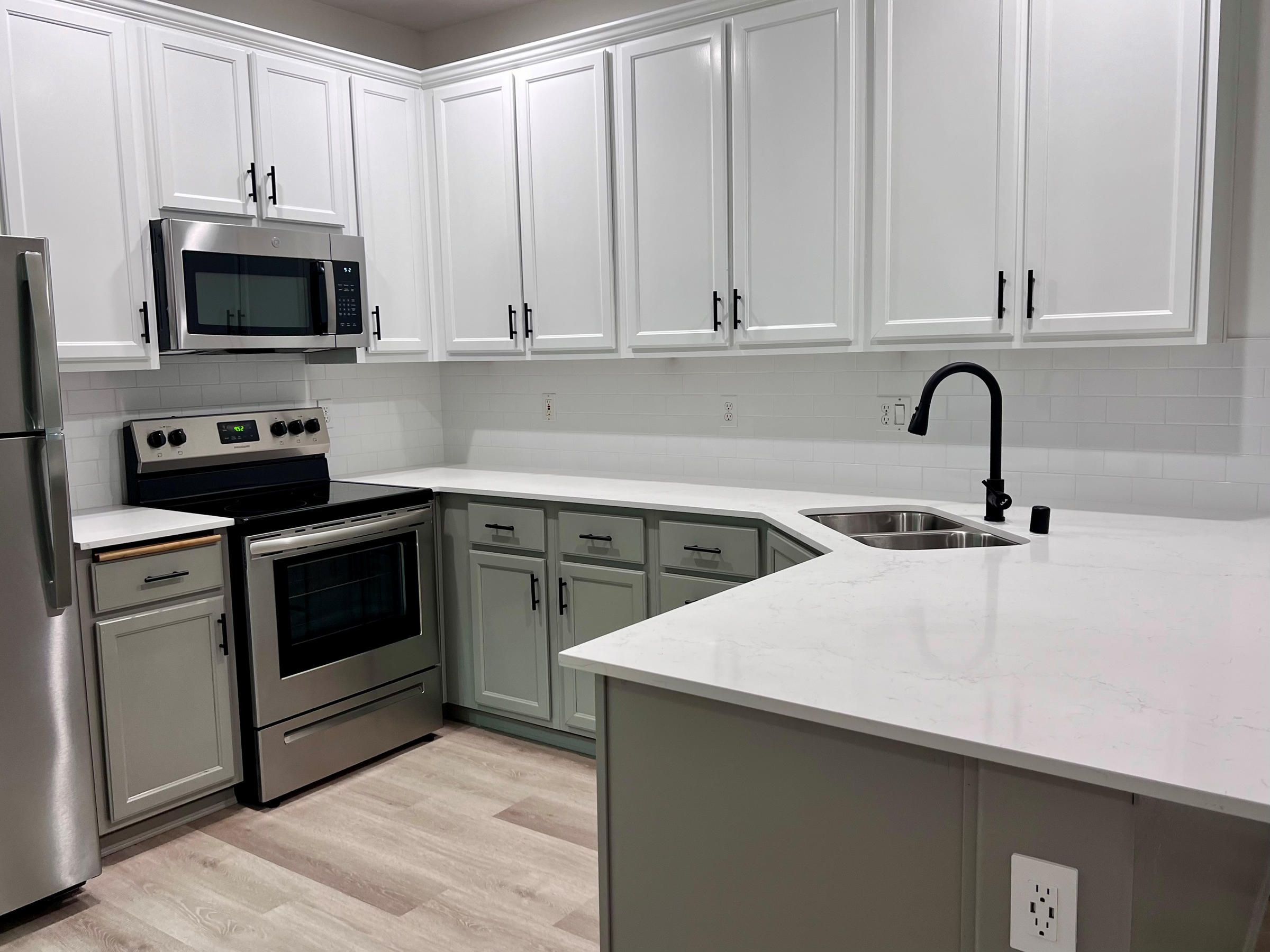 Modern kitchen with white upper cabinets, light gray lower cabinets, and stainless steel appliances.