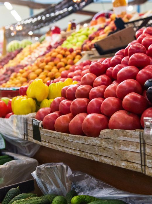 Fresh vegetables and fruits, including tomatoes, eggplants, and cucumbers, displayed at a busy market stall.