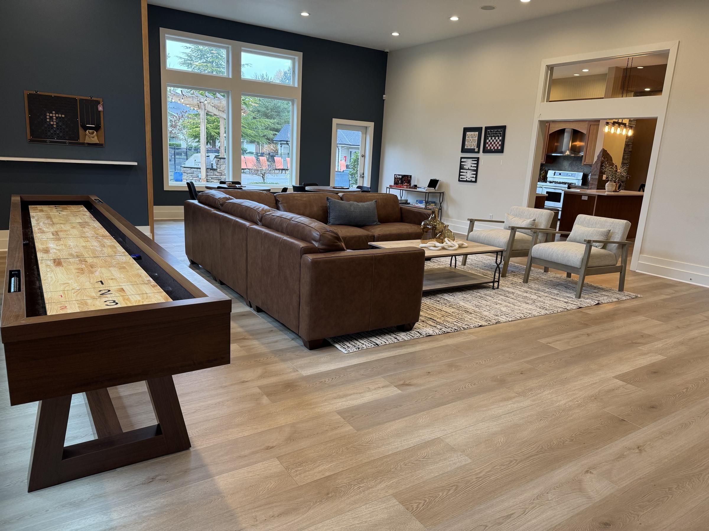Modern room with a brown leather sofa, shuffleboard table, and large windows facing outdoors.