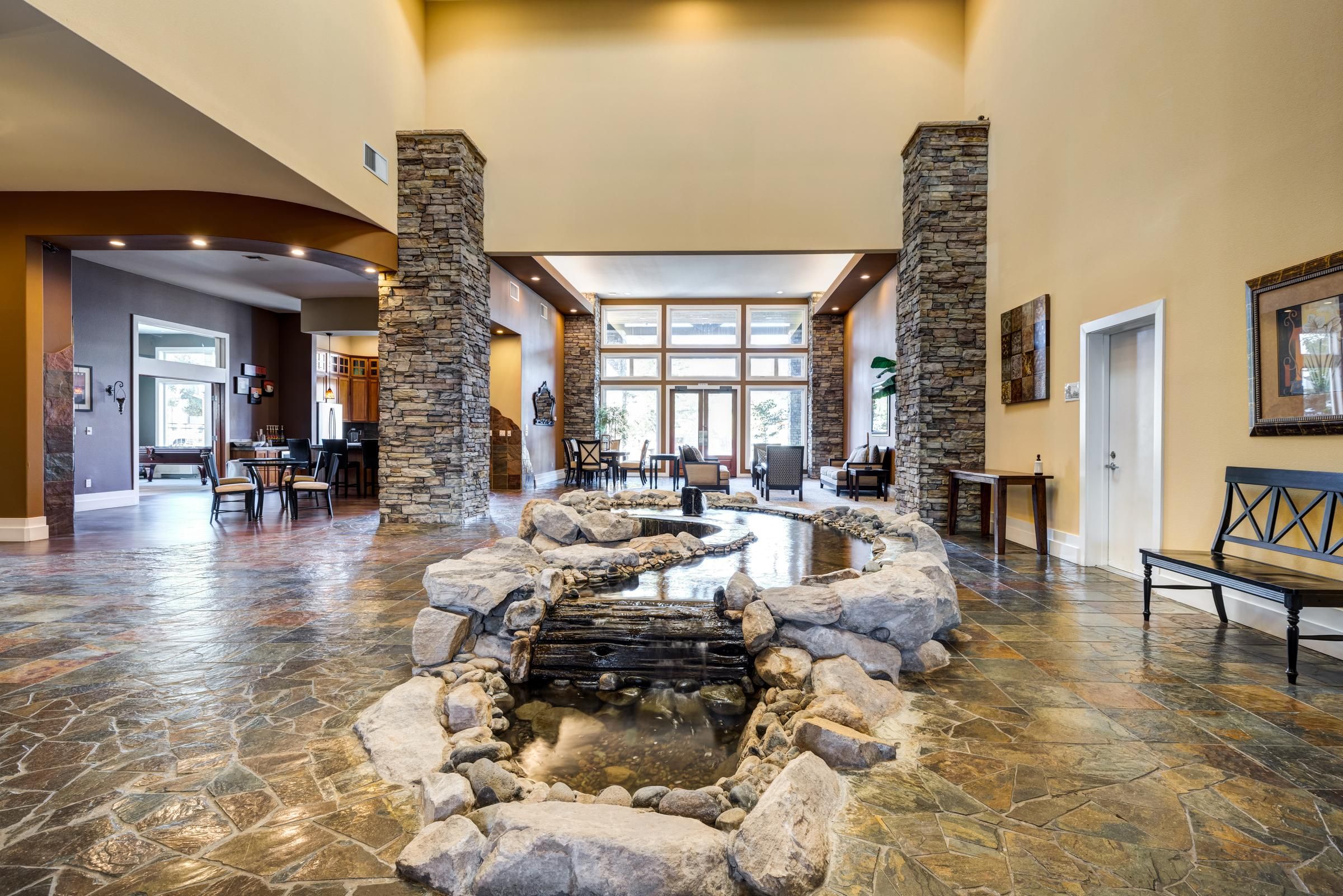 Spacious lobby with stone flooring, indoor rock pond, tall stone pillars, and large windows in the background.