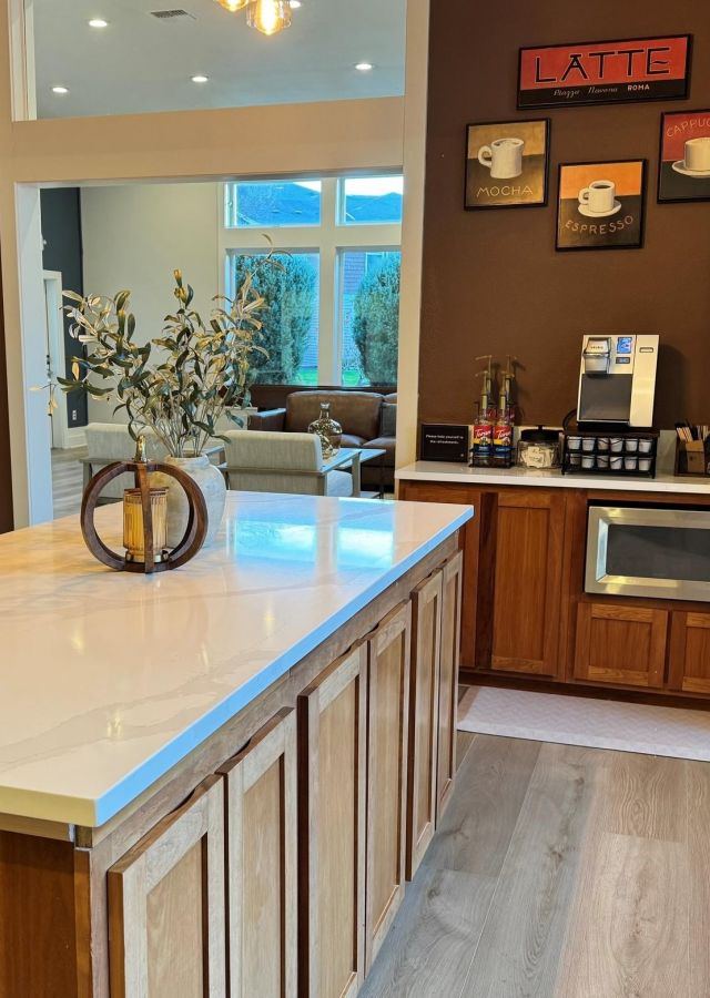 Modern kitchen with a marble island, coffee station, microwave, and stainless steel fridge.