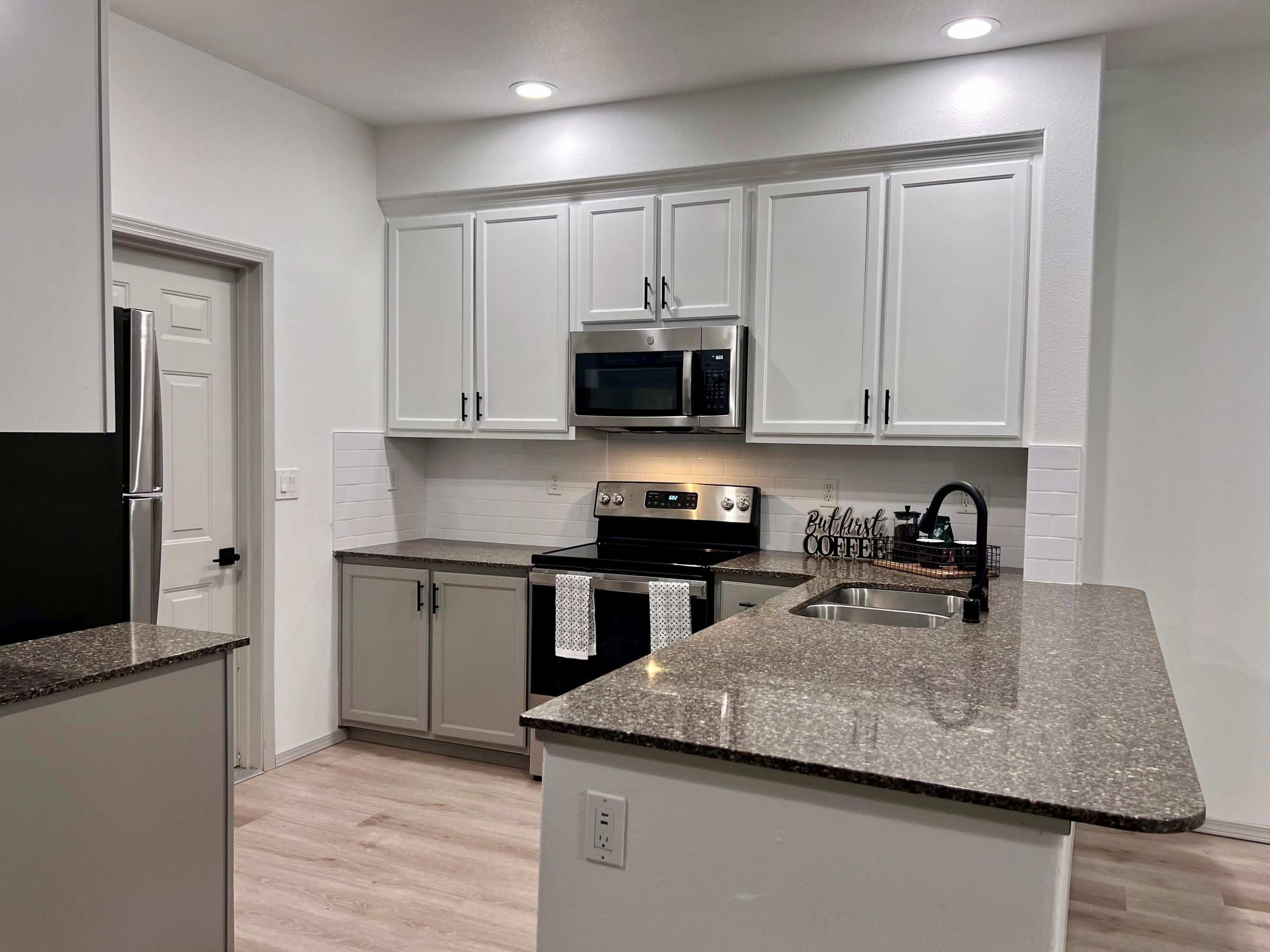 Modern kitchen with white cabinets, stainless steel appliances, and granite countertops under bright lighting.