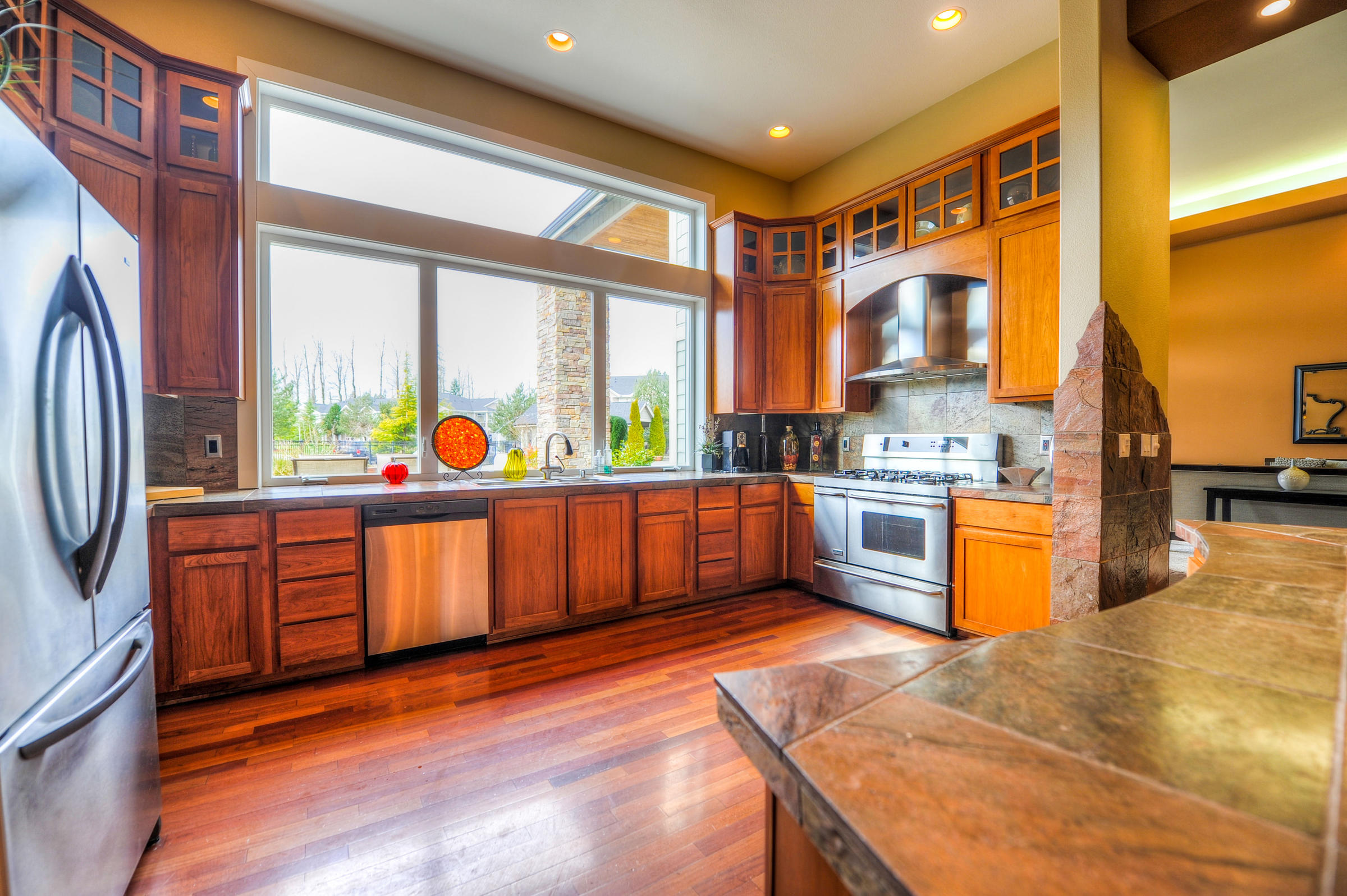 Modern kitchen with wooden cabinets, stainless steel appliances, and large window overlooking the outdoors.